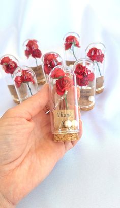 a hand holding a jar filled with red roses in it's top and the words thank you written on it