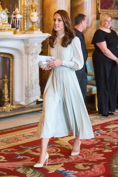 a woman in a long dress is walking through a room with other people standing around