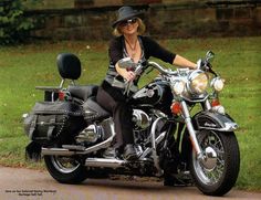 a woman riding on the back of a motorcycle down a road in front of some grass