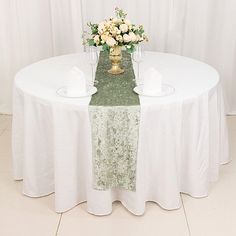 the table is set with white linens and gold vases filled with flowers on it