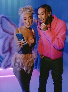 a man and woman standing next to each other in front of a blue wall with angel wings