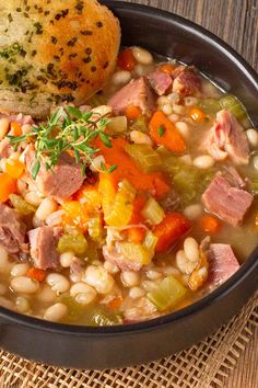 a bowl filled with ham and bean soup next to a piece of bread on top of a table