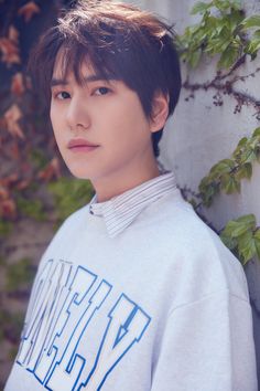 a young man standing in front of a wall with ivy growing up to his side