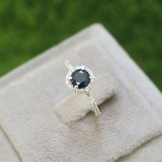 an engagement ring with a blue sapphire surrounded by diamonds on a white cloth in front of green grass