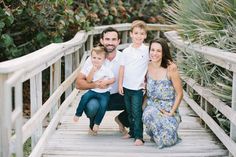 a family poses on a wooden bridge in front of some trees and bushes at the same time