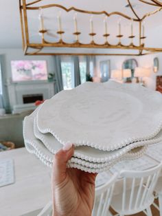 a person holding three white plates on top of each other in front of a chandelier