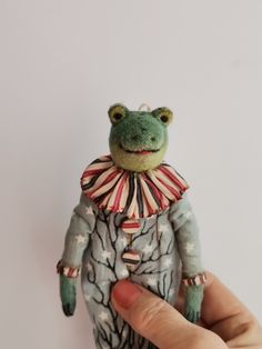 a hand holding a small stuffed frog wearing a red, white and blue striped shirt