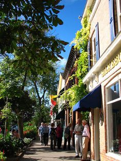 people are walking down the sidewalk in front of shops on a sunny day with blue skies