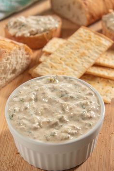 a white bowl filled with dip next to crackers and bread on a cutting board