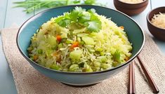 a bowl filled with rice and vegetables on top of a table next to chopsticks