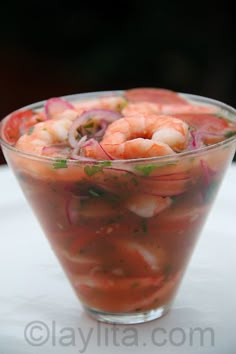 a glass bowl filled with shrimp salad on top of a white table next to a fork