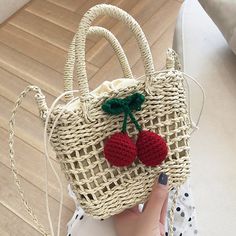 the straw bag has two cherries on it and is being held by a woman's hand