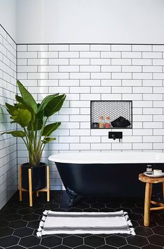 a black and white tiled bathroom with a plant in the bathtub next to it