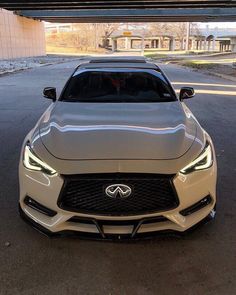 the front end of a white sports car parked in a parking lot under an overpass