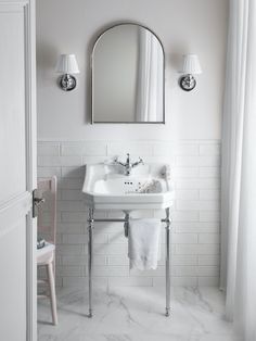 a white bathroom sink sitting under a mirror next to a pink chair in front of a window