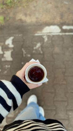 a person holding a cup of coffee in their hand on the street with brick pavement