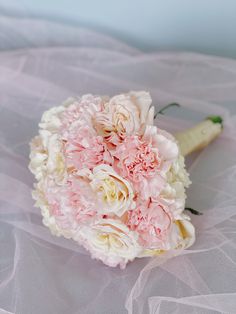 a bridal bouquet with pink and white carnations on a veiled surface