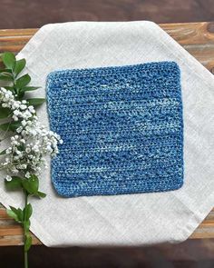 a blue crocheted dishcloth on top of a white napkin next to flowers