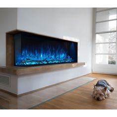 a dog laying on the floor in front of a wall mounted fireplace with blue flames