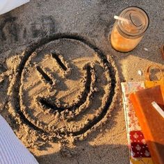 a smiley face drawn in the sand next to a jar and some other things on the ground