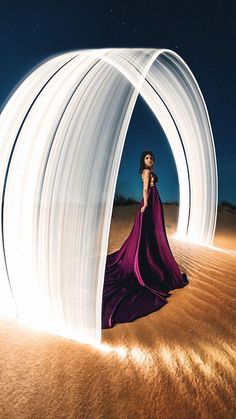 a woman in a long purple dress standing on sand