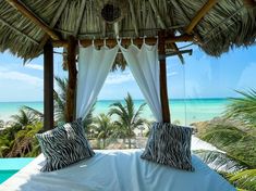 a bed with two zebra pillows on top of it next to the ocean and palm trees