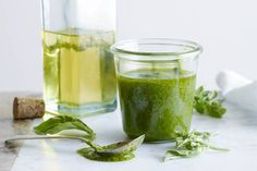 a glass jar filled with green liquid next to another container full of leaves and herbs