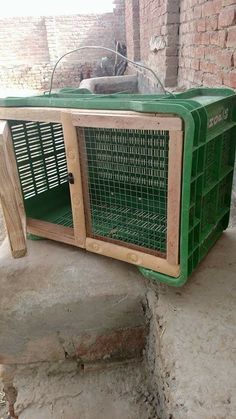 a green cage sitting on the side of a brick wall next to a cat laying in it