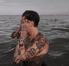 a man sitting in the water with tattoos on his face and hands behind his head