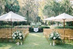 an outdoor ceremony set up with chairs and umbrellas in the grass, surrounded by greenery