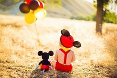 two children sitting in the grass with mickey and minnie mouse balloons flying above their heads