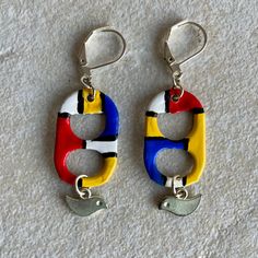 two pairs of colorful earrings hanging from silver hooks on a white carpeted surface,