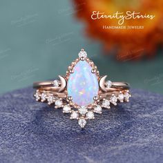 a white opal and diamond ring on top of a blue stone surface with an orange flower in the background