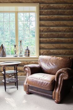 a leather chair sitting in front of a window next to a table with a vase on it