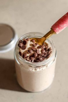 a jar filled with pudding and chocolate chips on top of a white table next to a spoon