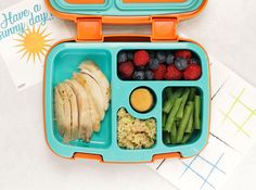 a blue lunch box filled with fruit and veggies next to a piece of paper