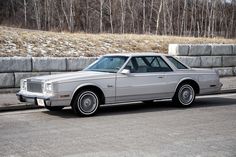 a silver car is parked on the side of the road in front of a stone wall