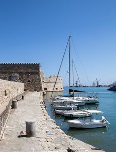 several boats are docked in the water next to an old brick wall and stone walkway