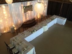 a banquet hall with tables and chairs set up for an event or function, decorated with white tablecloths and lights hanging from the ceiling