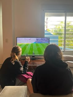 two women sitting in front of a flat screen tv watching a soccer game on the television