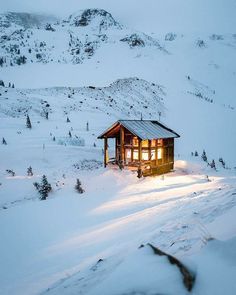 a small cabin sits on top of a snowy hill at night with the lights on