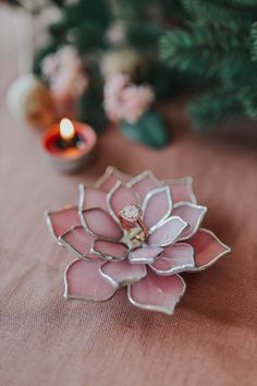 a pink flower brooch sitting on top of a table next to a lit candle