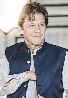 a man in a blue vest and white shirt is posing for the camera with his hands on his chest