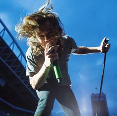 a man with long hair holding a microphone in front of an audience at a concert