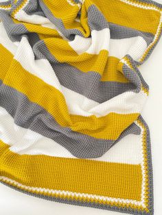 a yellow and grey striped blanket laying on top of a white table next to a cup