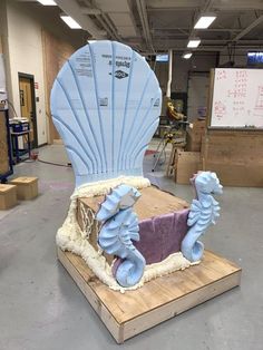 a large blue shell shaped chair sitting on top of a wooden platform in a warehouse