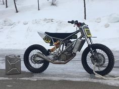 a dirt bike parked on the side of a road next to snow covered trees and bushes