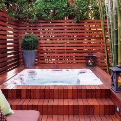 a hot tub sitting on top of a wooden deck next to a bamboo planter