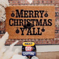 merry christmas y'all next day shopping door mat on wooden floor with white pom - poms