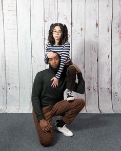 a man sitting on top of a woman's head in front of a wooden wall